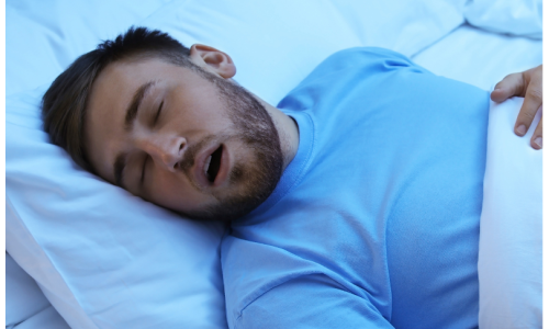 Man sleeping on his side in bed with his mouth open, appearing to snore, highlighting the potential need for a CPAP machine to assist with breathing during sleep